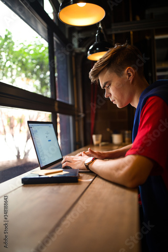 Fashionable hipster guy freelance social media content writer connected to public wifi via laptop computer while sitting in coffee shop interior. Man college student online learning via notebook