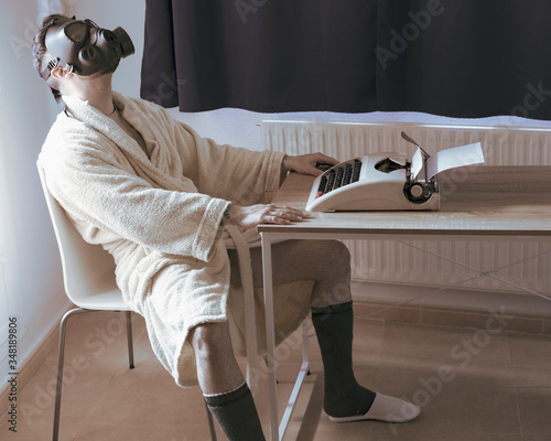 man in bathrobe working from home on typewriter, with gas mask. quarantine concept