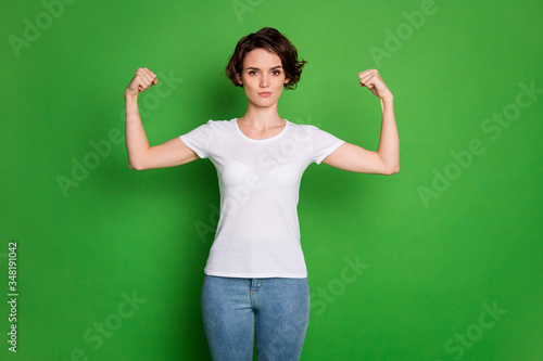 Photo of attractive self-confident lady wavy bobbed hairdo demonstrating two perfect shape biceps can beat any guy wear casual white t-shirt blue jeans isolated green color background