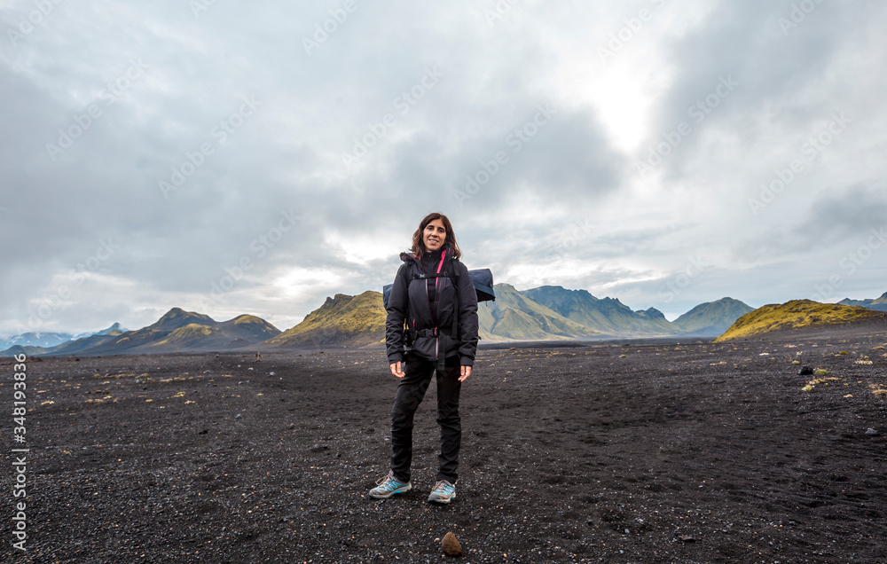 A young woman in volcanic ash and a green mountain in the background on the 54 km trek from Landmannalaugar, Iceland