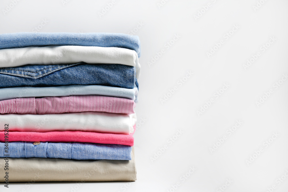 Stack of colorful perfectly folded clothing items. Pile of different pastel color shirts, sweaters isolated and other garments on white background. Close up, copy space. Stack of colorful perfectly folded clothing items. Pile of different pastel color shirts, sweaters isolated and other garments on white background. Close up, copy space.