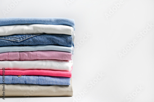 Stack of colorful perfectly folded clothing items. Pile of different pastel color shirts, sweaters isolated and other garments on white background. Close up, copy space.
