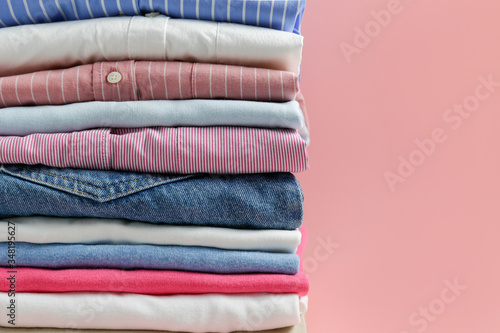 Stack of colorful perfectly folded clothing items. Pile of different pastel color shirts and sweaters isolated on pale pink background. Close up, copy space.