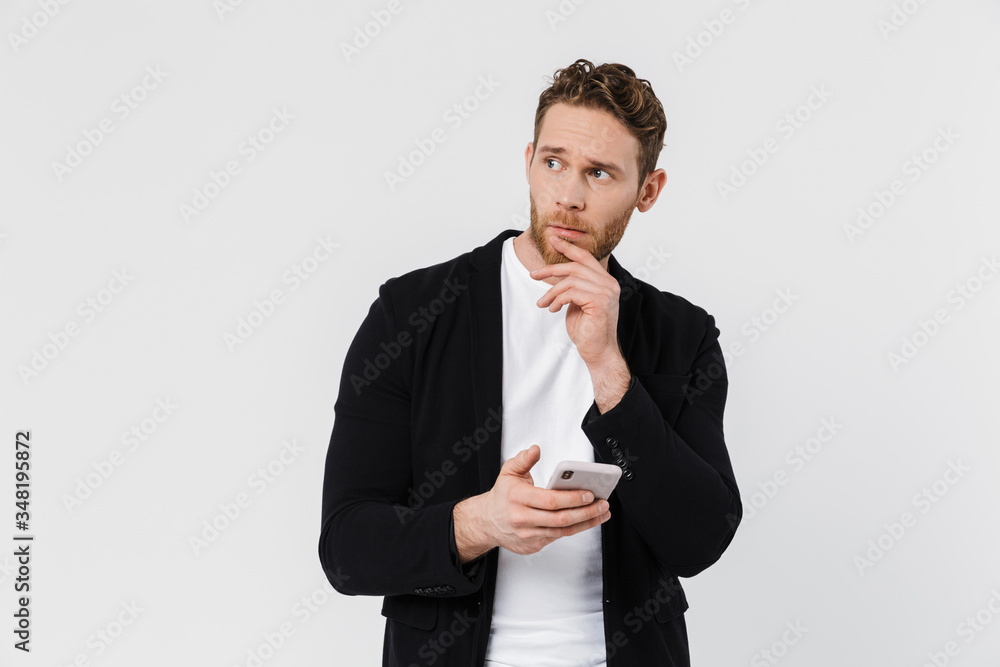 Image of handsome serious man in jacket thinking and using smartphone Image of handsome serious man in jacket thinking and using smartphone
