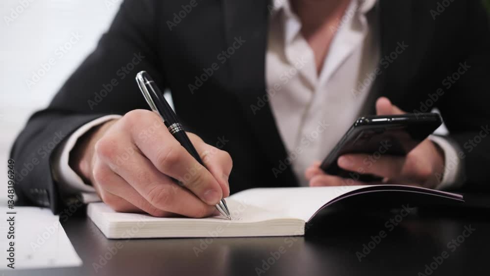 Close up view of Young businessman makes calculations on the phone and writes data in a notebook. Close up view of Young businessman makes calculations on the phone and writes data in a notebook.
