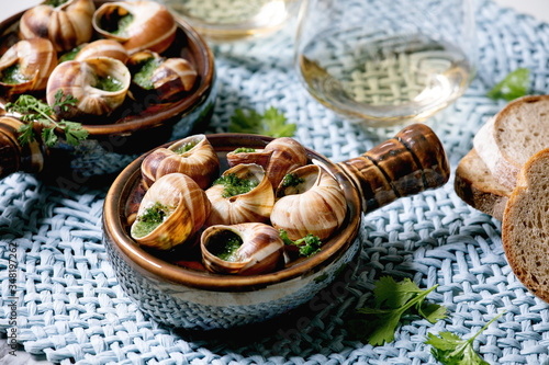 Escargots de Bourgogne - Snails with herbs butter, gourmet dish, in traditional ceramic pan with coriander, bread, glass of white wine on blue straw napkin. Close up