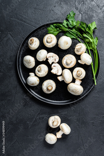 Raw mushrooms champignon on a plate. Black background. Top view. Space for text