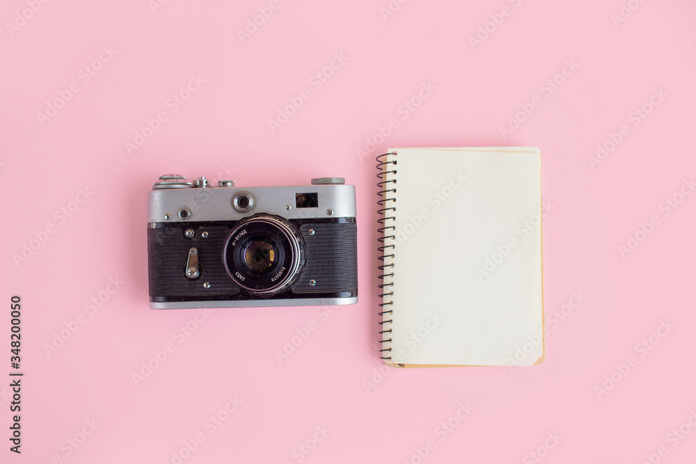 Fototapeta premium Modern workspace concept with photo camera, notebook on pink background with copyspace. Office desktop. Top view