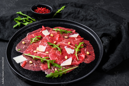 Beef carpaccio on black plate with parmesan sauce, cheese and arugula. Black background. Top view