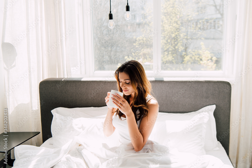 attractive positive girl drinking coffee in bed in morning during self isolation attractive positive girl drinking coffee in bed in morning during self isolation