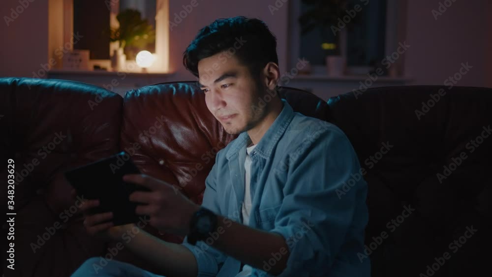 Handsome Asian men playing game on tablet at home on sofa. Handsome Asian men playing game on tablet at home on sofa.