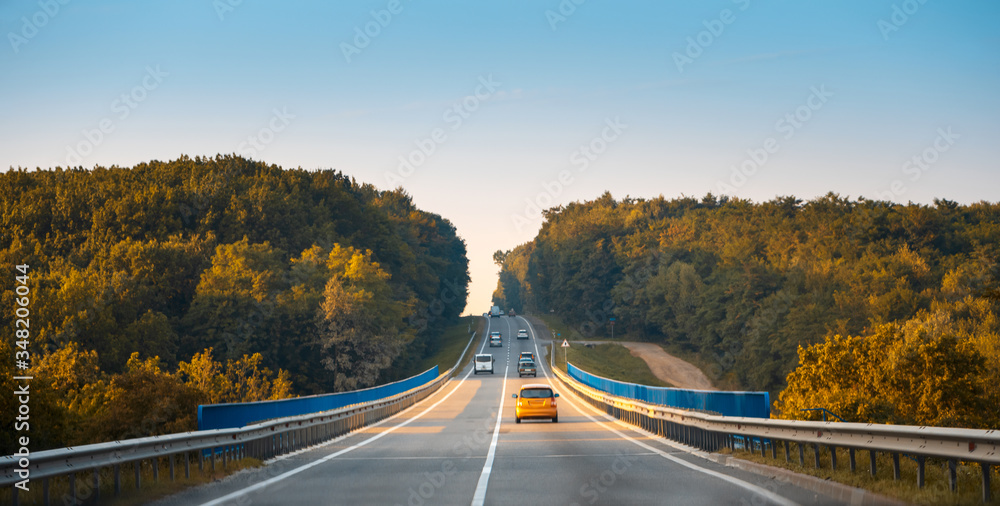 Traffic in high speed on a highway through rural landscape on sunset.