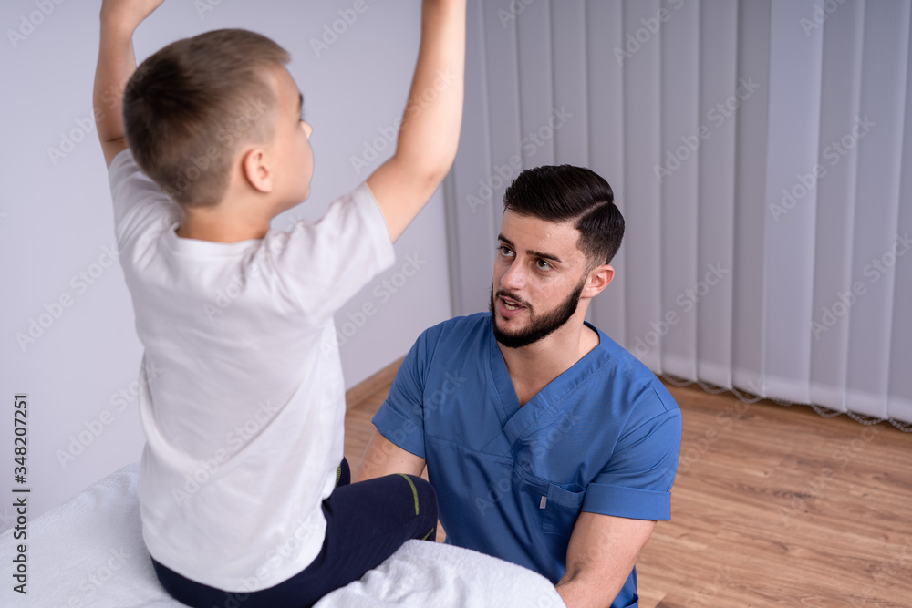 Fototapeta premium Boy sits on a special couch, beside him, sat the doctor in the form of doctors, concept of treatment and rehabilitation