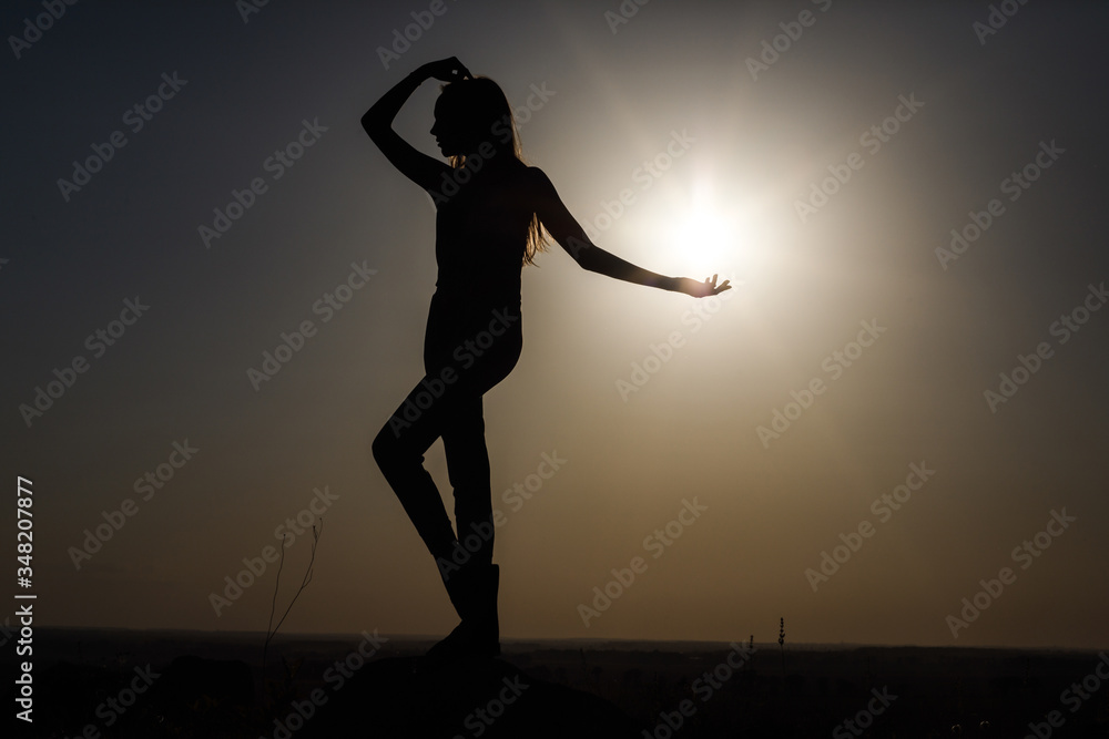 Silhouette of a girl at sunset standing on a rise.