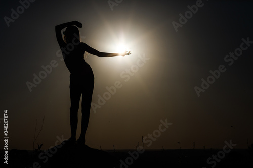 Silhouette of a girl at sunset standing on a rise. © gladiusstock
