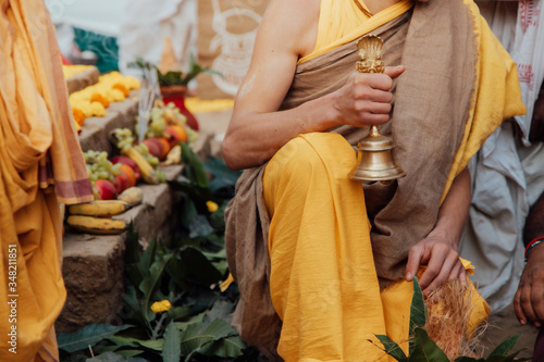 young Brahman Brahmachari holds a bell in his hands during Yagya a fire flame ritual of hindu pooja performating during sacred traditional Vedic ceremony.