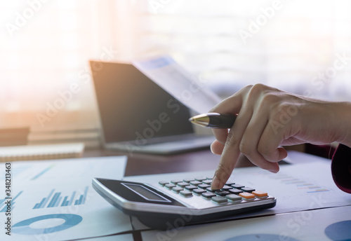 Business office worker or accountant hand holding pen and press to button calculator to calculate finance report  profit loss account  statistics analytical research. Background sunlight copy space.