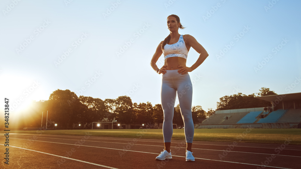 Beautiful Fitness Woman in Light Blue Athletic Top and Leggings is Catching Her Breath and Posing in a Stadium. She was Training on a Warm Summer Afternoon and Doing Her Routine Workout. 
