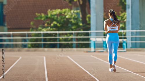 Beautiful Fitness Woman in Light Blue Athletic Top and Leggings Jogging in a Stadium. She is Running on a Warm Summer Afternoon. Athlete Doing Her Routine Sports Practice on a Track.