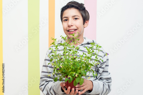 Cute young boy holding a flowerig pot in on a colorful striped backgroung. Great