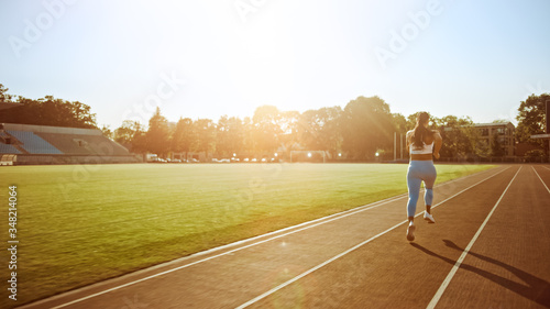 Beautiful Fitness Girl in Light Blue Athletic Top and Leggings Jogging in the Stadium. She is Running on a Warm Summer Afternoon. Athlete Doing Her Routine Sports Practice on a Track.