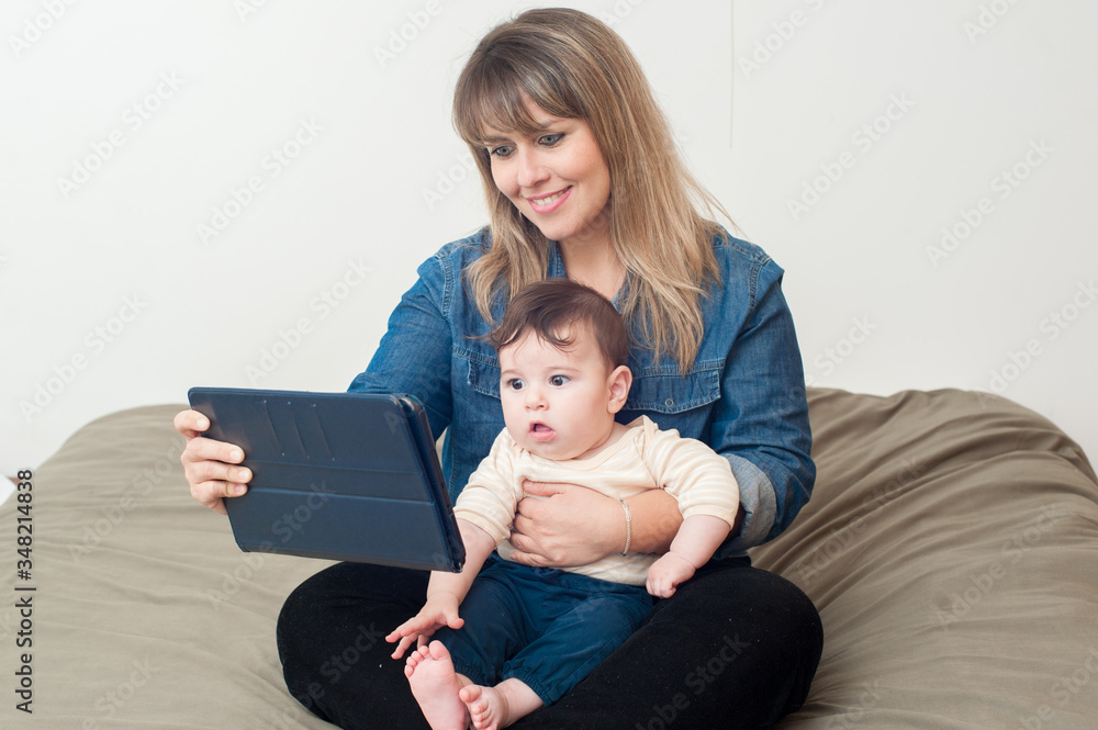 Mom using the tablet im bed and holding her newborn baby on her lap. Mom using the tablet im bed and holding her newborn baby on her lap.