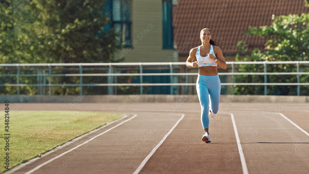 Beautiful Fitness Woman in Light Blue Athletic Top and Leggings Jogging in a Stadium. She is Running on a Warm Summer Afternoon. Athlete Doing Her Routine Sports Practice on a Track.
