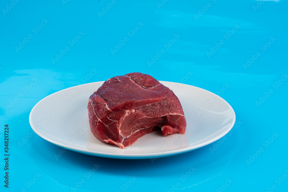 piece of raw beef meat tenderloin on a white plate on a blue background piece of raw beef meat tenderloin on a white plate on a blue background