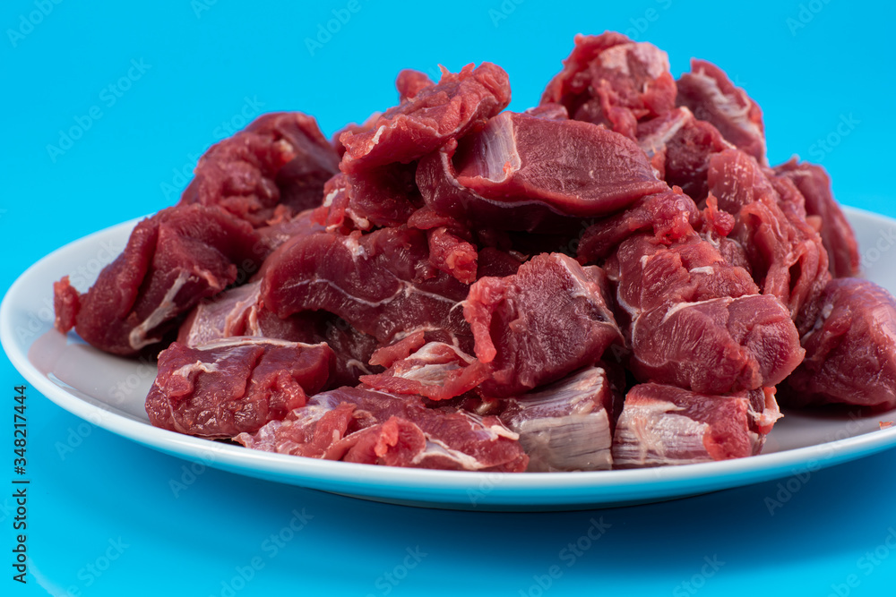 chopped small pieces of raw beef meat, tenderloin on a white plate on a blue background