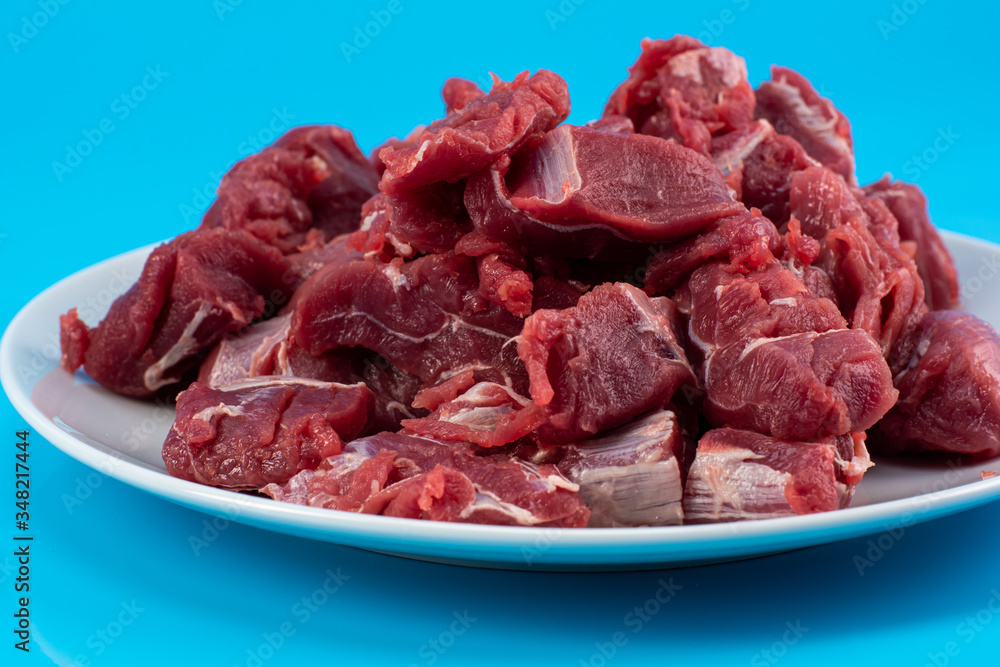 chopped small pieces of raw beef meat, tenderloin on a white plate on a blue background chopped small pieces of raw beef meat, tenderloin on a white plate on a blue background