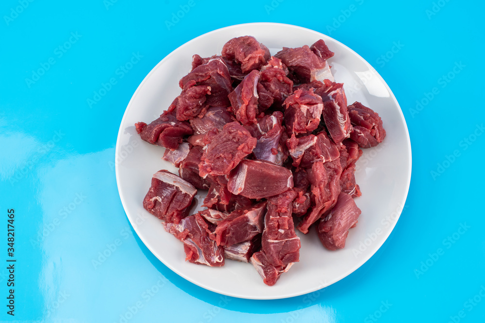 chopped small pieces of raw beef meat, tenderloin on a white plate on a blue background chopped small pieces of raw beef meat, tenderloin on a white plate on a blue background