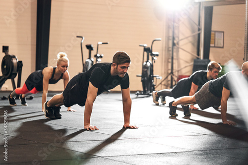 Group of fit people doing pushups together at the gym photo