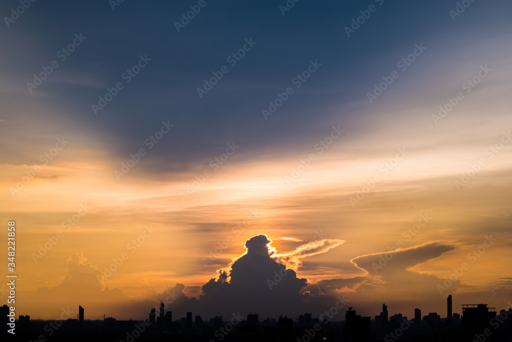 Naklejka premium Silhouette cityscape and many buildings towers with beautiful sunset with twilight sky and cloud. sunset and light rays from clouds shining to sky. Heaven in nature.