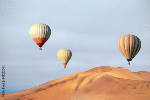 Colored hot air balloons flying over the sand dunes at sunset. Africa, Namibia