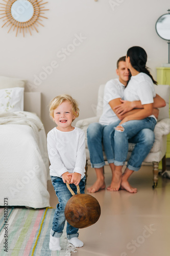 Joyful blond boy holds stylish decor in the foreground while parents cuddle on the background. photo