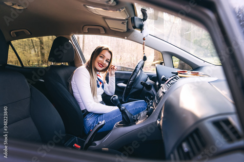 Girl dressed in a white shirt sitting behind the wheel of a new