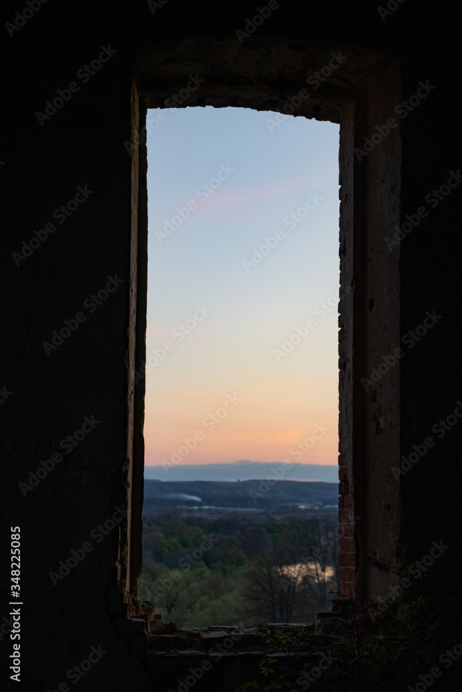 View of the hill and sunset through the window opening of an old abandoned church