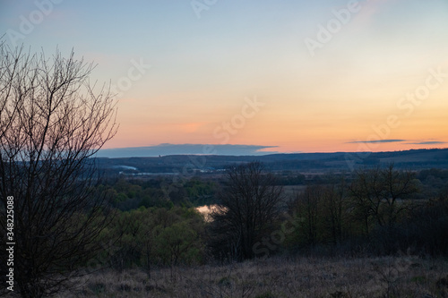 View of the surroundings with forests and the river from a high hill at sunset.
