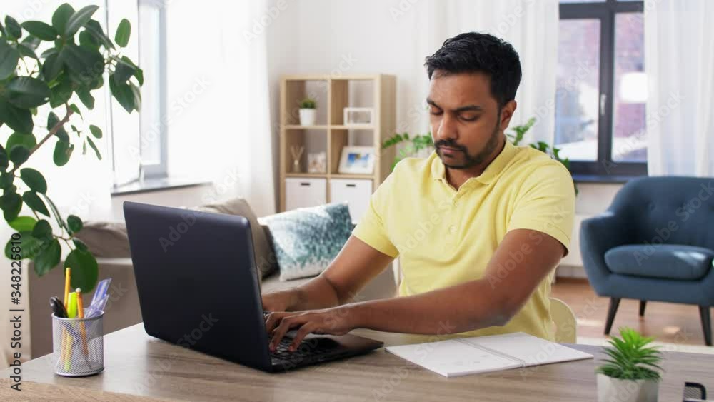 remote job, technology and people concept - young indian man with notebook and laptop computer working at home office remote job, technology and people concept - young indian man with notebook and laptop computer working at home office