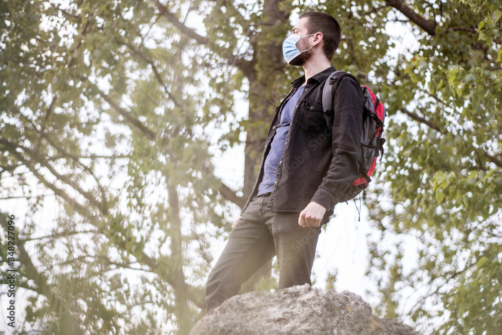 A young bearded caucasian man in medical mask standing in the nature, raising his head to the top and enjoying A young bearded caucasian man in medical mask standing in the nature, raising his head to the top and enjoying