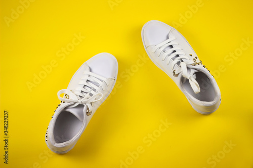 A pair of new white women's sneakers on a yellow background. The view from the top