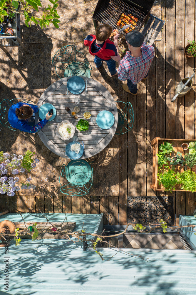 Fototapeta premium Top view, at home a family prepares a barbecue on a terrace, the father shows his son how to take care of the grills.