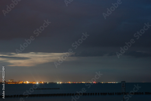 Night by the sea. No wave on the sea. Beach scene in summertime. Evening on the coast. Sand and water. Silence. Pacified mood. Nobody. Seascape. Lights of city away. 