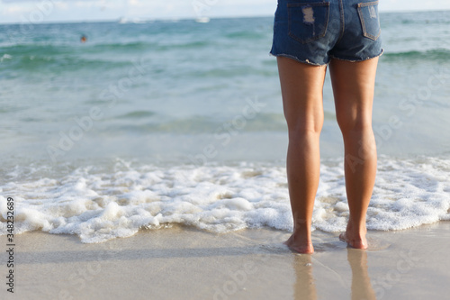 Woman legs standing on white sand beach.