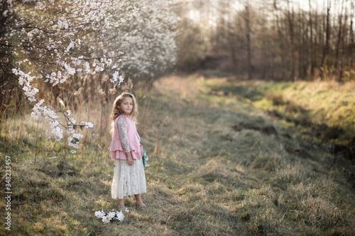 fair-haired girl of 7 years old, standing in the field. near a blossoming apple tree. holding a book in his hands. dressed in a long lace white dress and a pink vest. field in the background