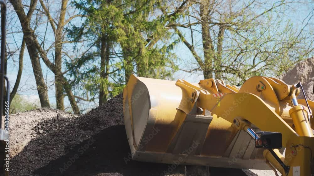 4K video. A yellow bulldozer on a clear day picks up rubble in pick-ups. Close-up. 4K video. A yellow bulldozer on a clear day picks up rubble in pick-ups. Close-up.