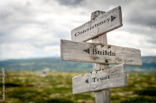consistency builds trust text engraved on old wooden signpost outdoors in nature. Quotes, words and illustration concept. photo