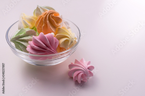 Multi-colored small meringues in a glass plate on a white background. Copy space.