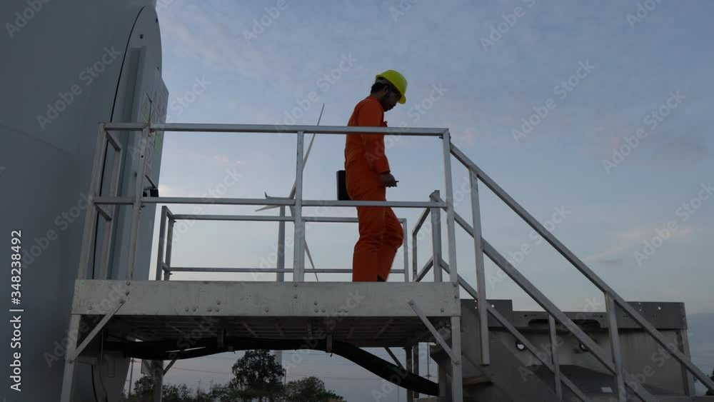 Asian man engineer working and holding the report at wind turbine farm Power Generator Station on mountain,Thailand people Asian man engineer working and holding the report at wind turbine farm Power Generator Station on mountain,Thailand people