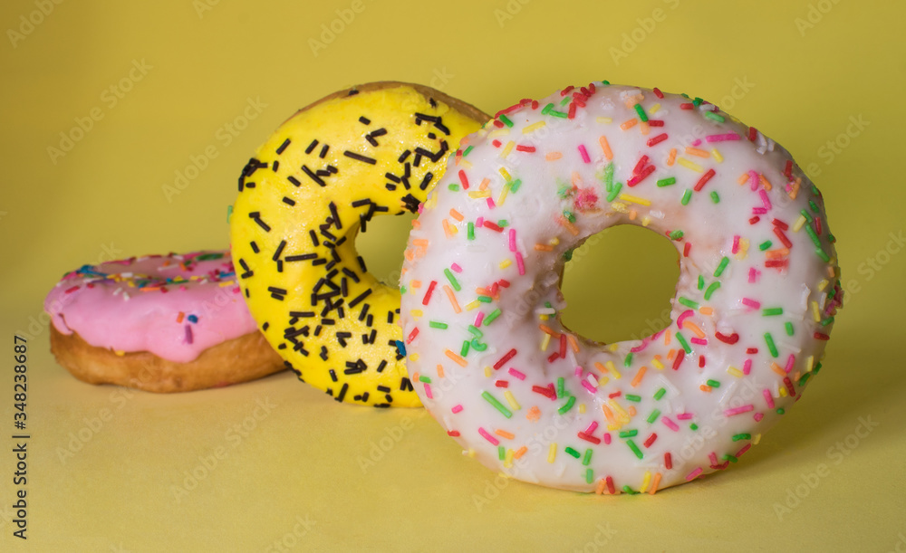 Three doughnuts, two lying on top of each other, and one standing sideways, on a yellow background, beautiful food with powder